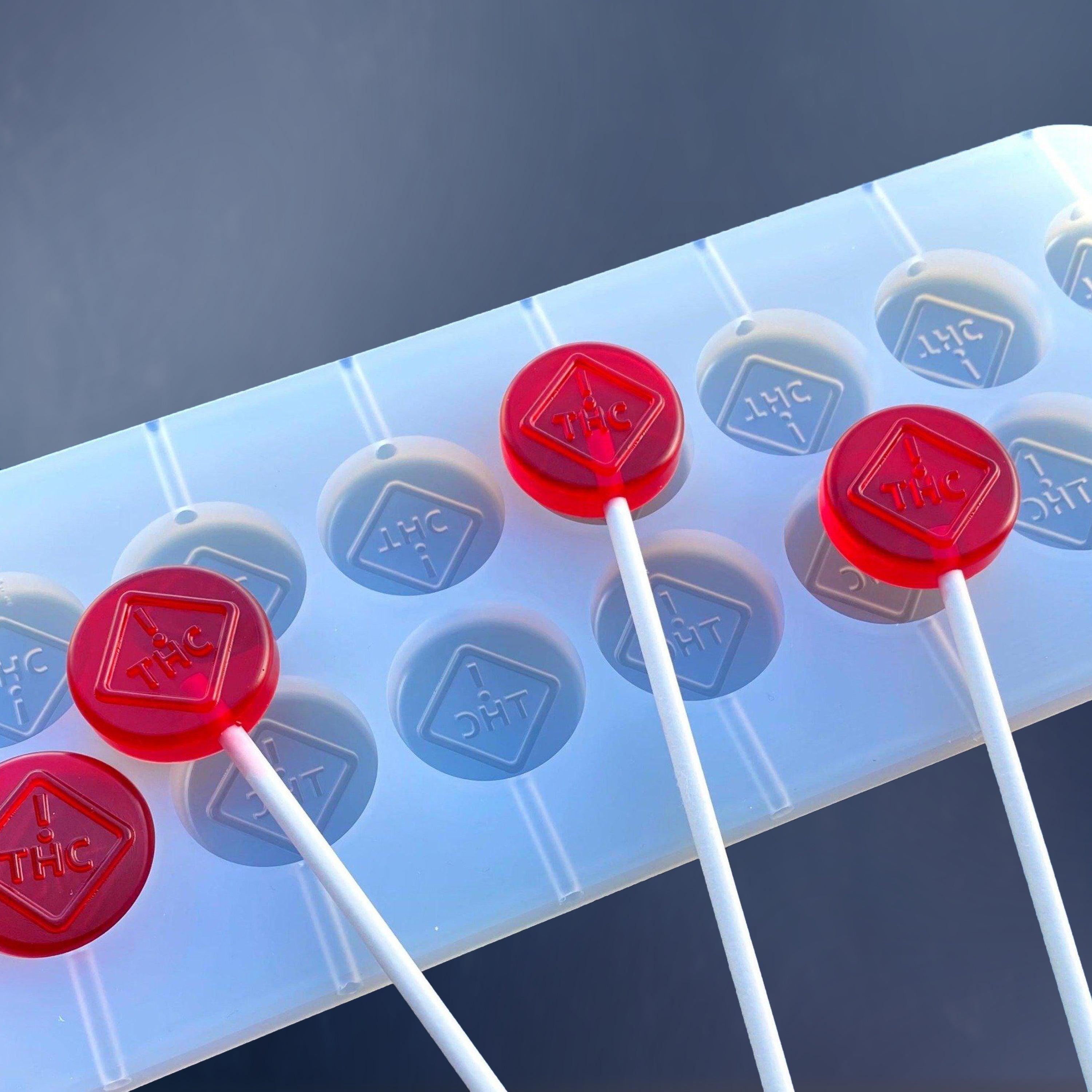 Three red THC-labeled lollipops rest on a white silicone mold with matching THC markings against a blue background.