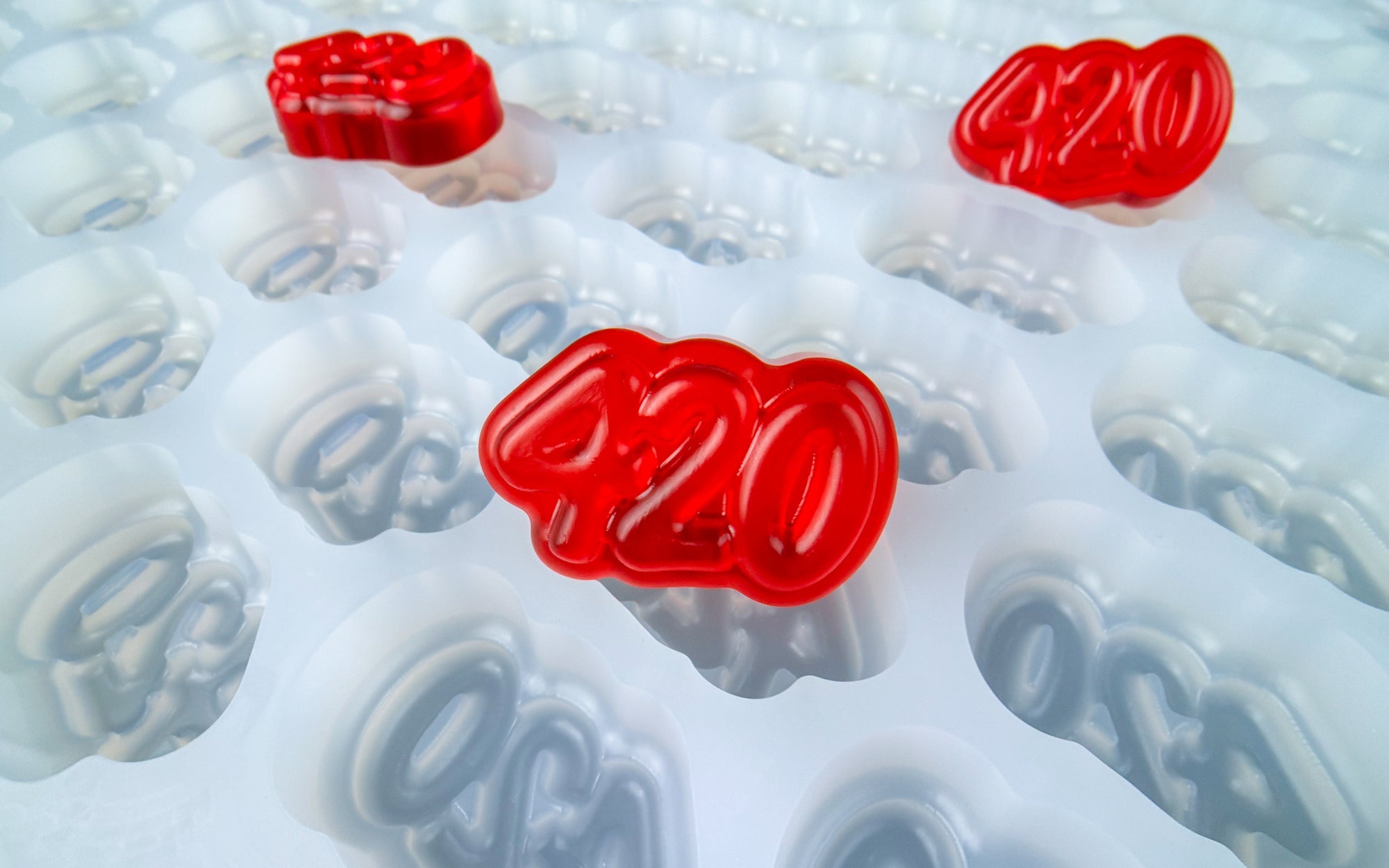 Red translucent gummies labeled "CBN" rest on and inside a white plastic tray with corresponding "CBN" labels, set against a plain blue background.