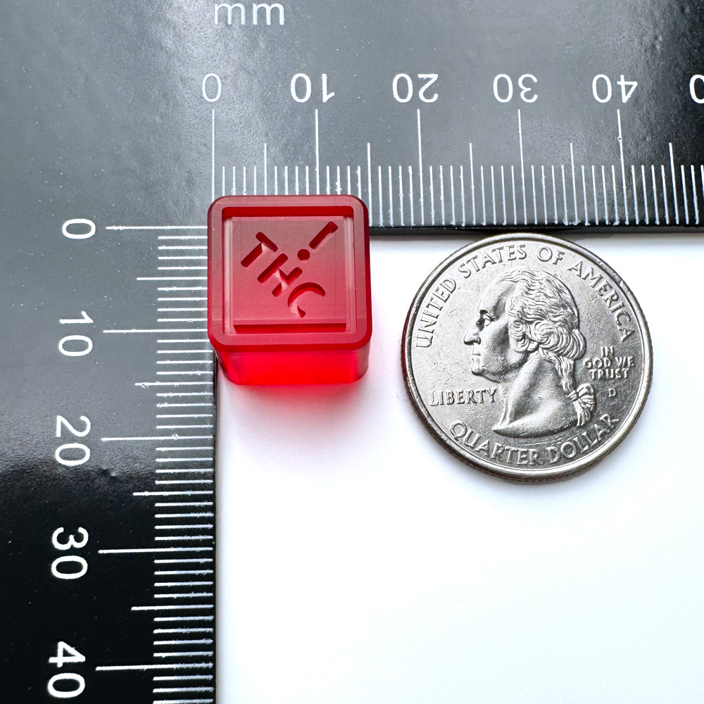 A red gummy with a THC label sits near a U.S. quarter and mm ruler, highlighting the precision of the Vector Molds 2 mL Square Gummy Mold—CO, OH, NM & FL THC Logo Flood + Scrape version with 430 cavities in food-grade platinum silicone.