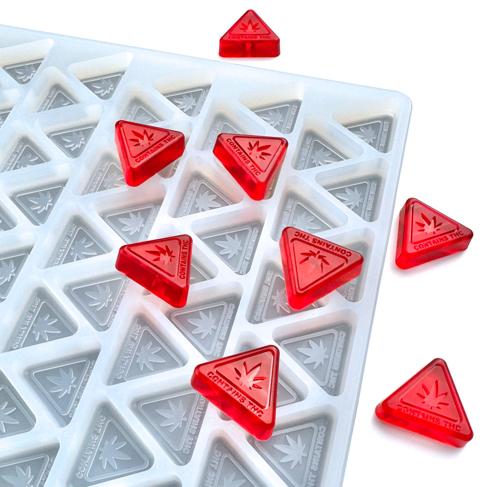 The Vector Molds 3 mL MA, ME, & RI State THC Logo Triangle Mold (half sheet, 200 cavities) holds multiple red, translucent triangle gummies marked "Contains THC" with a cannabis leaf symbol.