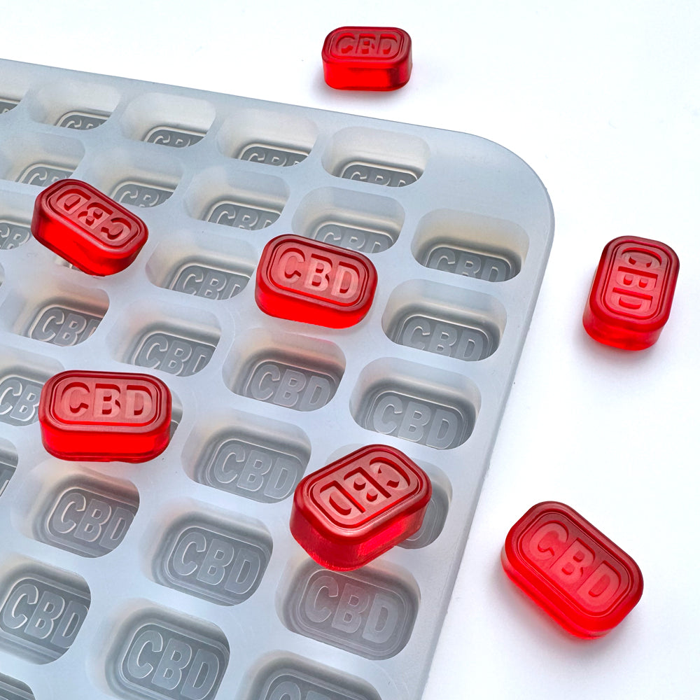 The Vector Molds 4 mL Brick Gummy Mold - Half Sheet with 186 cavities holds multiple red, rectangular gummies, with a few gummies placed on the white surface next to the mold.