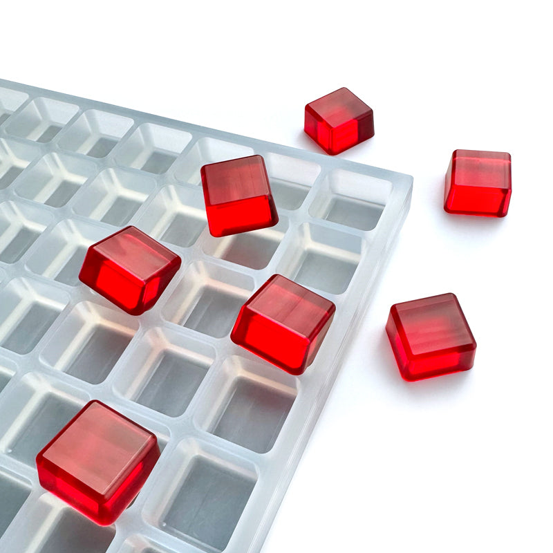 The Vector Molds 5 mL Square Gummy Mold - Sharp Half Sheet with 192 cavities holds several red, translucent, square gummies, some nestled in the mold while others rest on a nearby white surface.
