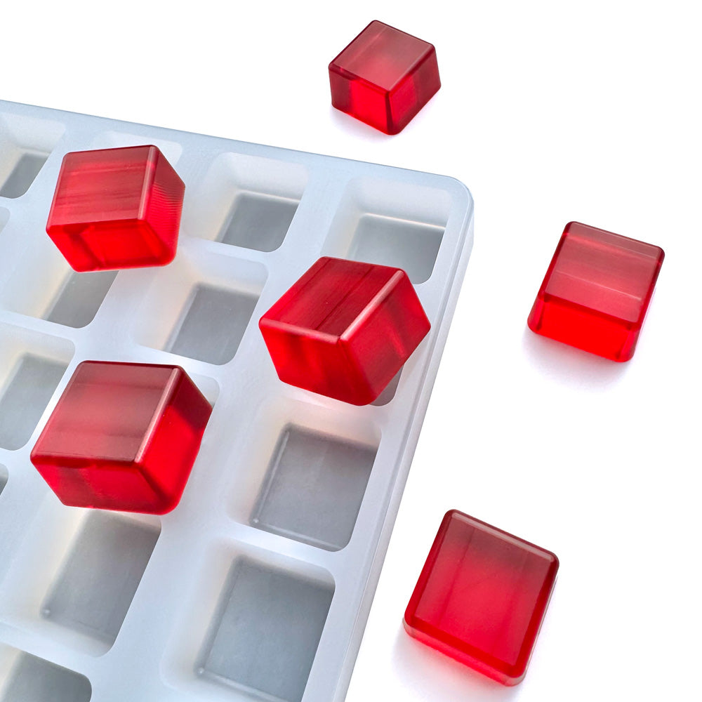 The Vector Molds 8 mL Square Gummy Mold - Universal Depositor (112 cavities), an FDA-approved white silicone tray, holds and displays several red, translucent square gummies, with some placed outside on a white surface.