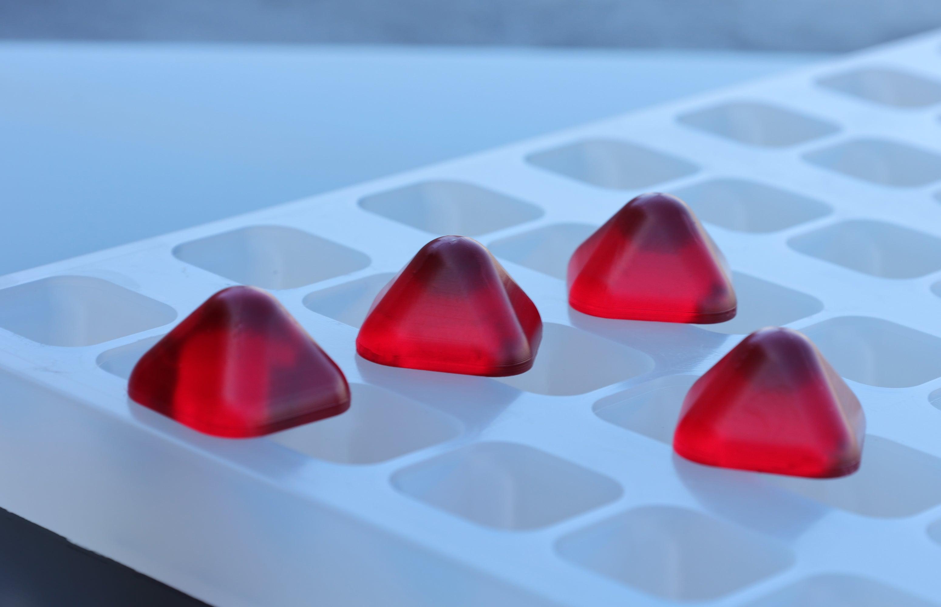 Close-up of custom food-grade silicone pyramid gummy mold, 3ml Vector Piramid shape with sharp geometry and smooth finish, shown with glossy red gummies