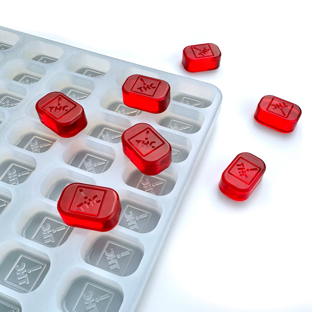 A white tray displays several red, rectangular gummies stamped with a THC symbol, each made using the Vector Molds 4 mL Brick Gummy Mold—CO, OH, NM & FL THC Logo Mold with 152 cavities; some gummies rest beside the tray.