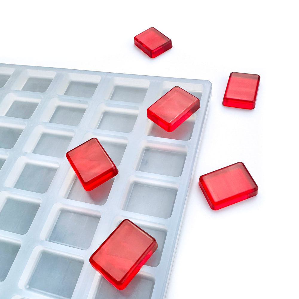 The Vector Molds 3 mL Rectangular Gummy Mold - Universal Depositor with 136 cavities holds translucent red gummies, while others are scattered on the white surface.