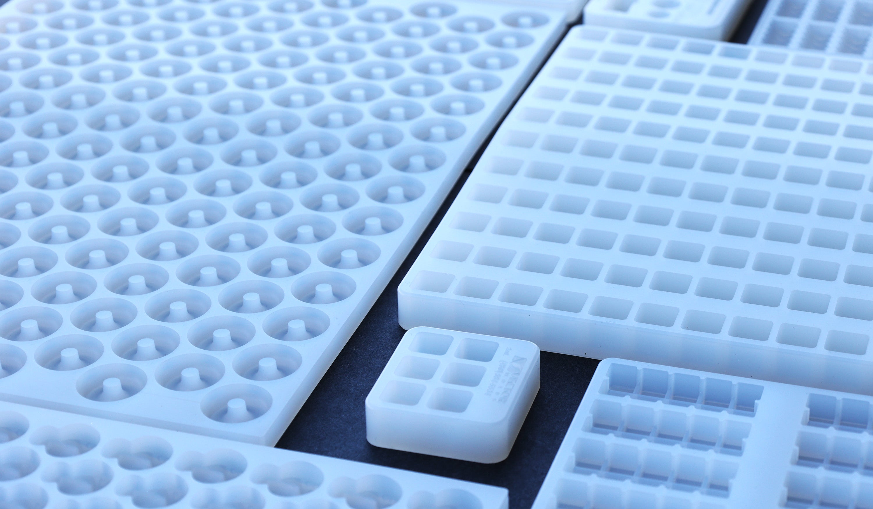 Close-up view of various white silicone or plastic molds with different shapes and cavity sizes arranged closely together.