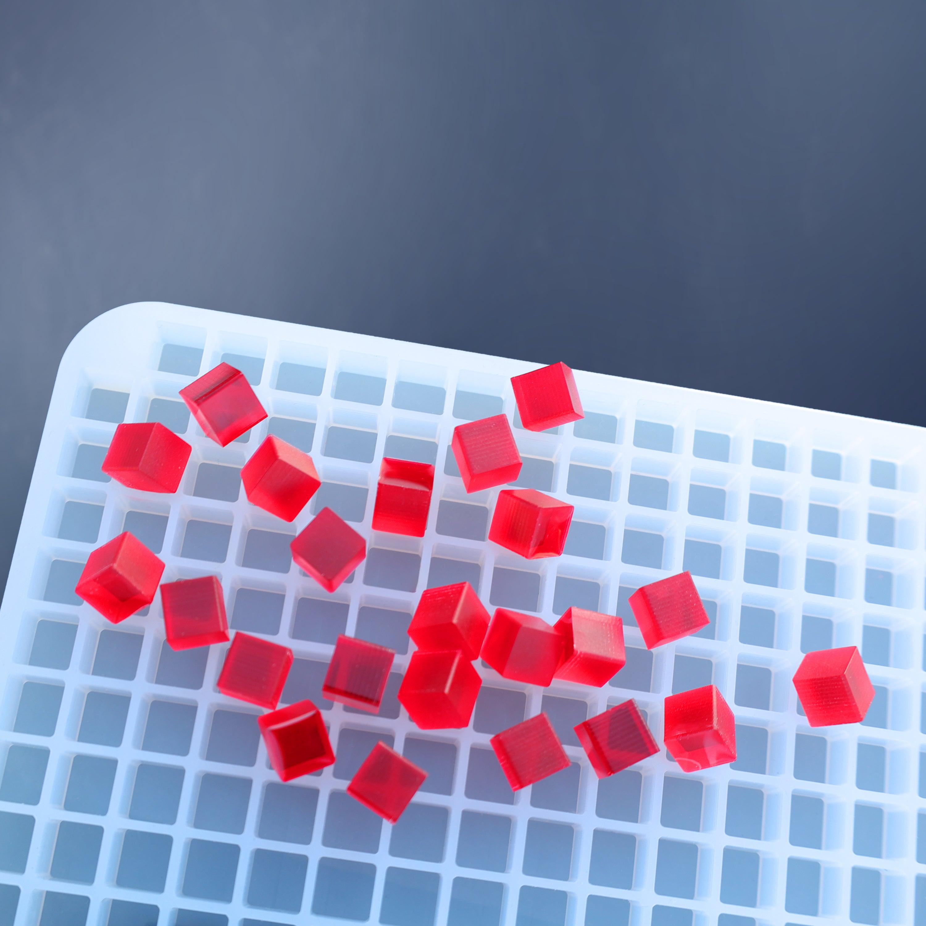 Red gelatin cubes, made with the 1 mL Square & Cube Gummy Mold - Full Sheet (1781 Cavities) by Vector Molds, are scattered on a white plastic grid tray against a blue background.