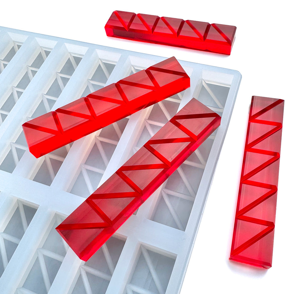 Four translucent red resin bars with triangular patterns rest on a Vector Molds 15 mL Stick Breaker Bar Gummy Mold - Half Sheet, which features 52 rectangular slots and geometric designs.