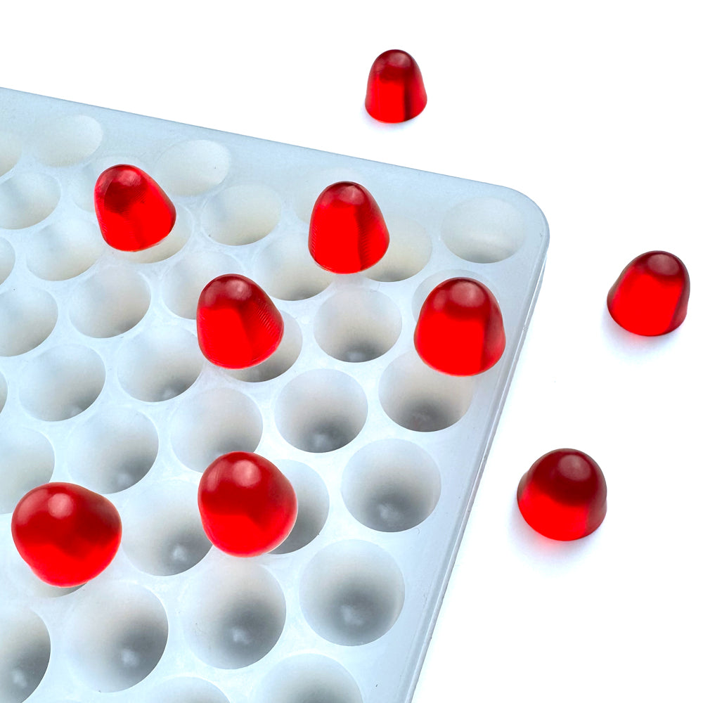 The Vector Molds 2.2 mL Gumdrop Mold - Half Sheet with 340 cavities holds red gummies, with some candies placed outside the white silicone tray on a white surface.