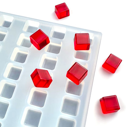 A white Vector Molds 3 mL Square Gummy Mold - Depositor (152 cavities) is partially visible with several red translucent cubes on and beside it, set against a white background.