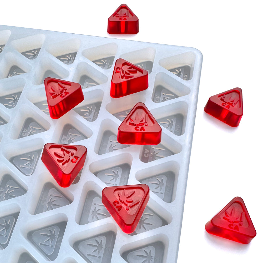 The Vector Molds 3 mL Triangle Gummy Mold - CA THC Logo Mold - Half Sheet features 224 white, food-grade silicone cavities, each forming red triangular gummies embossed with a cannabis leaf and "CA." Some gummies are displayed outside the mold.