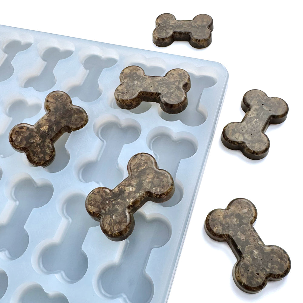 A silicone mold with cavities shaped like bones, filled with gummy treats, on a white background. Perfect precision molds for creating accurately dosed treats for you pets. Peanut butter, Ground meat, or oatmeal snacks can be made and baked in this food grade mold.