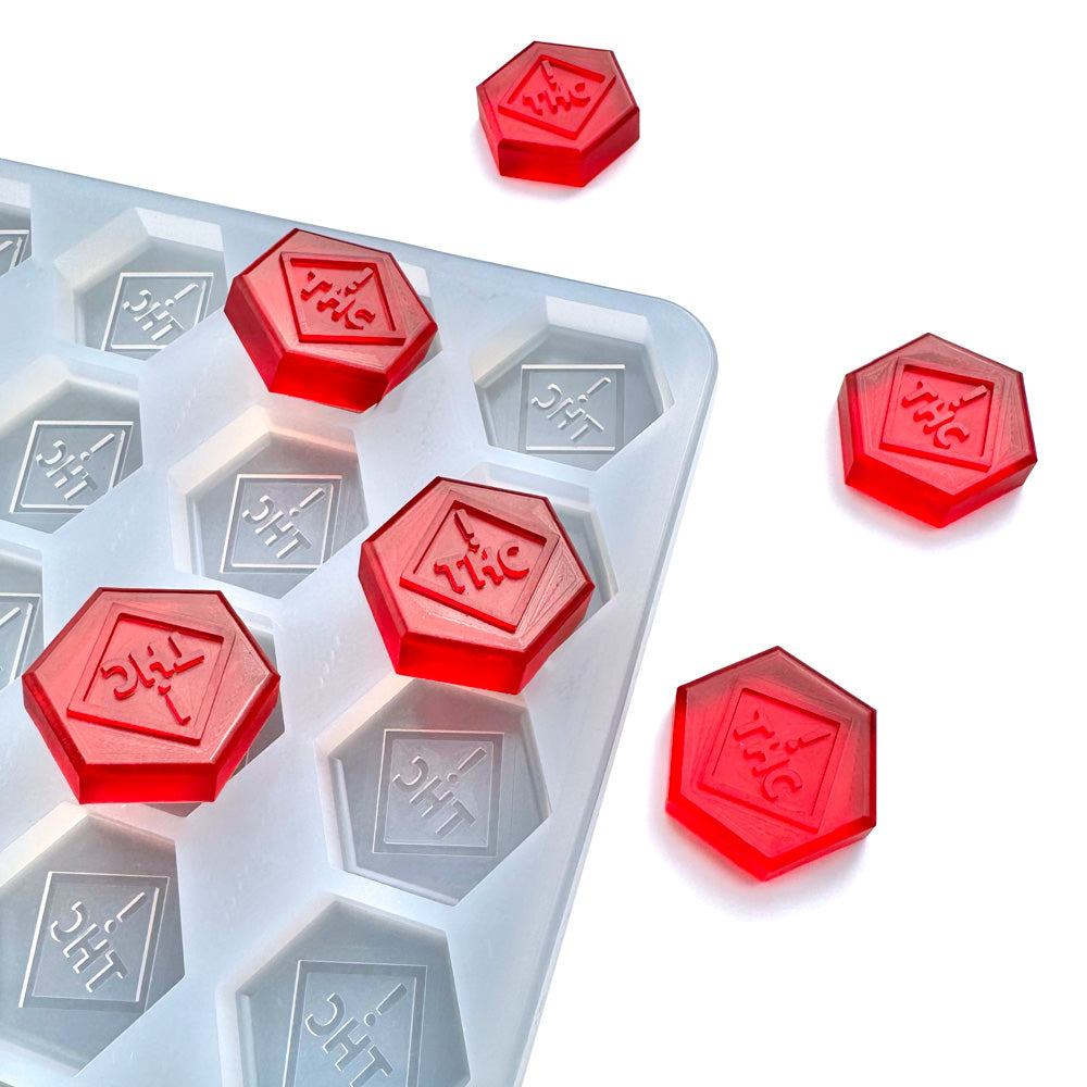 A white FDA-approved Vector Molds 4.6 mL Hexagon Gummy Mold with 104 cavities, featuring the CO, OH, NM & FL THC logo, is shown with several red THC-marked hexagonal gummies on and around the mold.