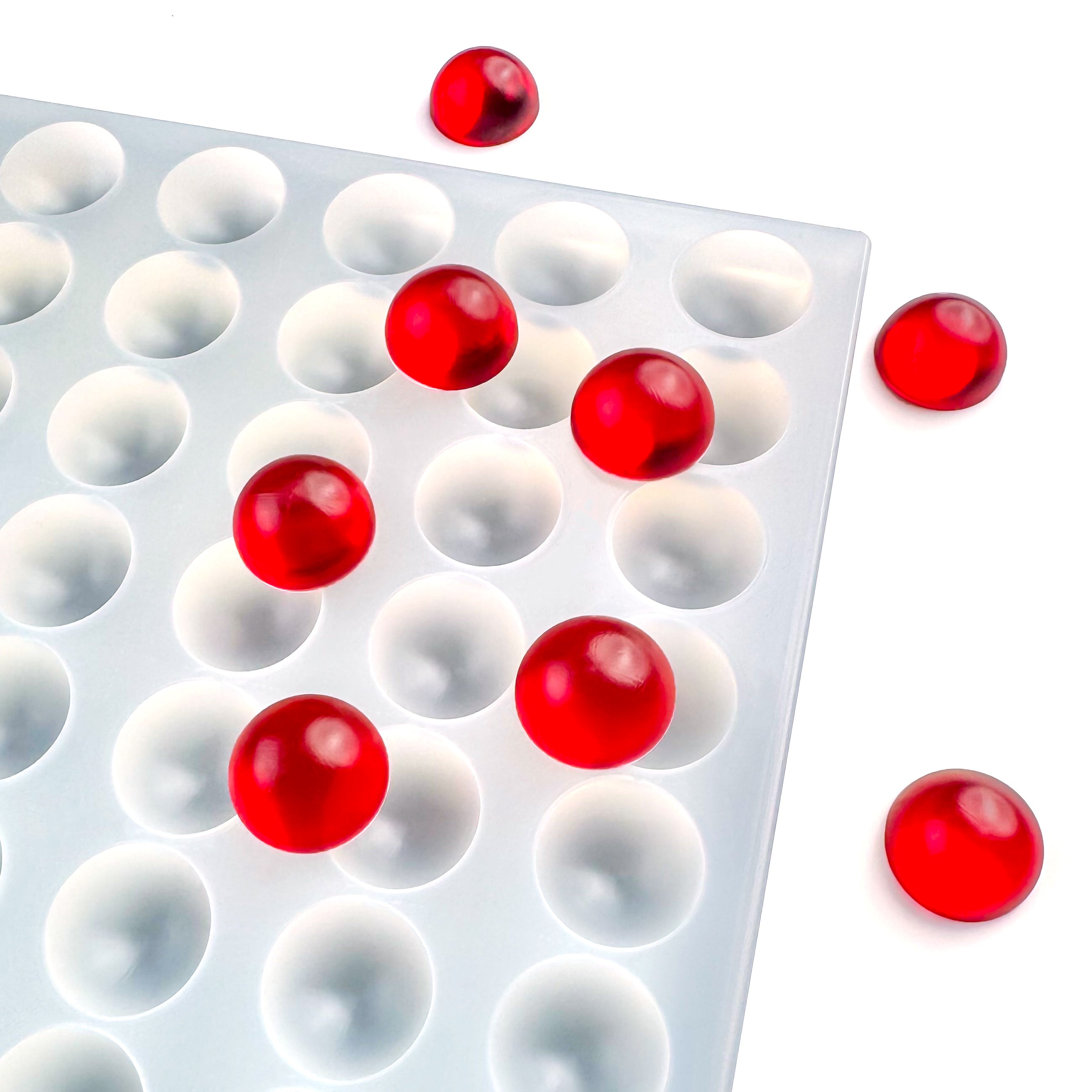 The Vector Molds 4 mL Bon Bon Gummy Mold - Universal Depositor (112 Cavities) holds several red gummies, with a few placed outside the tray on a white surface.