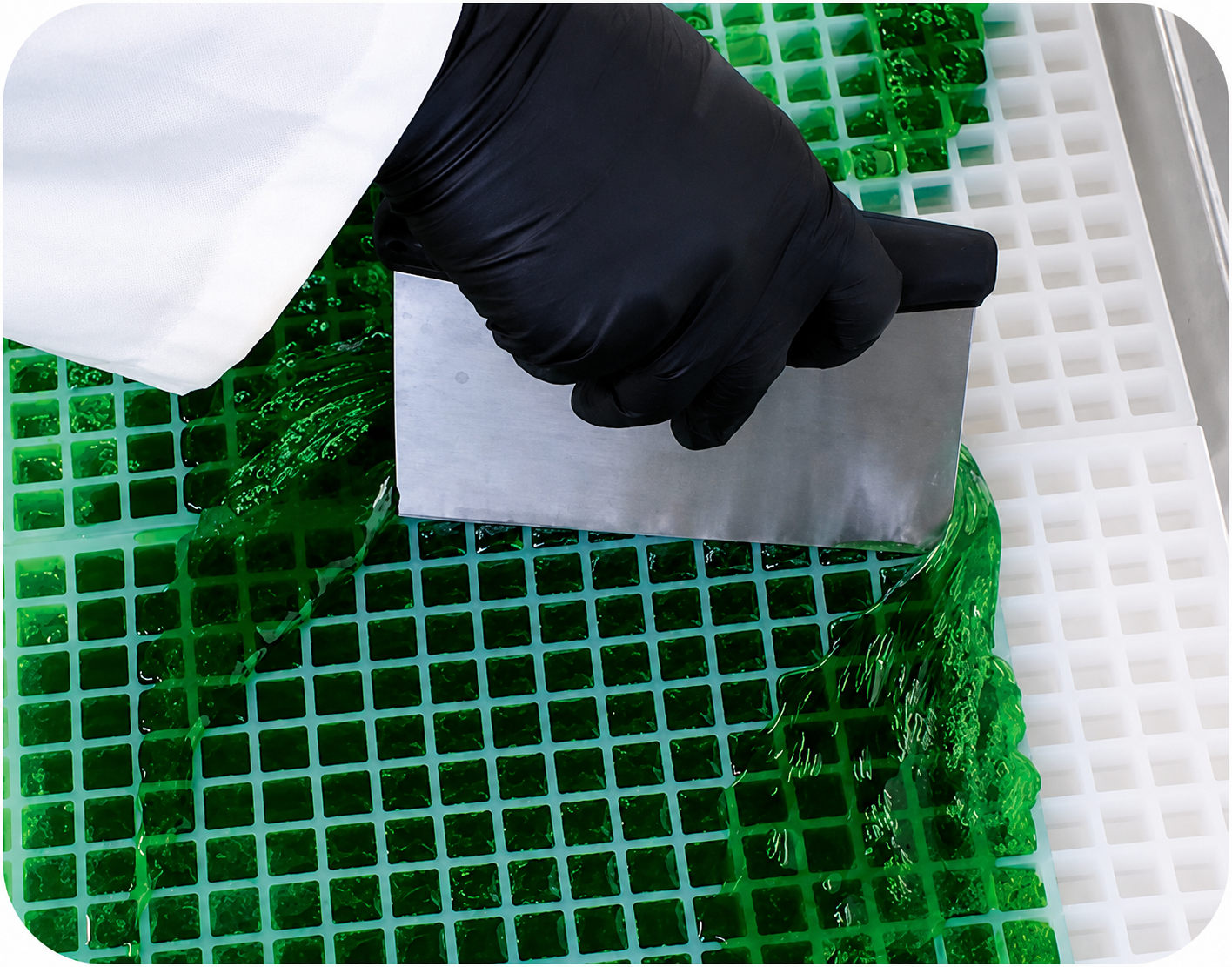 Candy mixture being scraped across a Vector Molds mold, showing the flood-and-scrape hand-pour method for smooth, efficient, and even cavity filling in production.