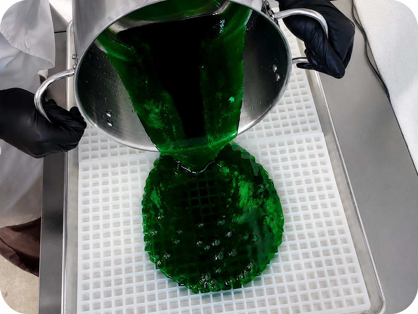 Hand-pour production process showing a half sheet Vector Molds mold being flooded with warm confectionery mixture for efficient candy making and consistent cavity filling.