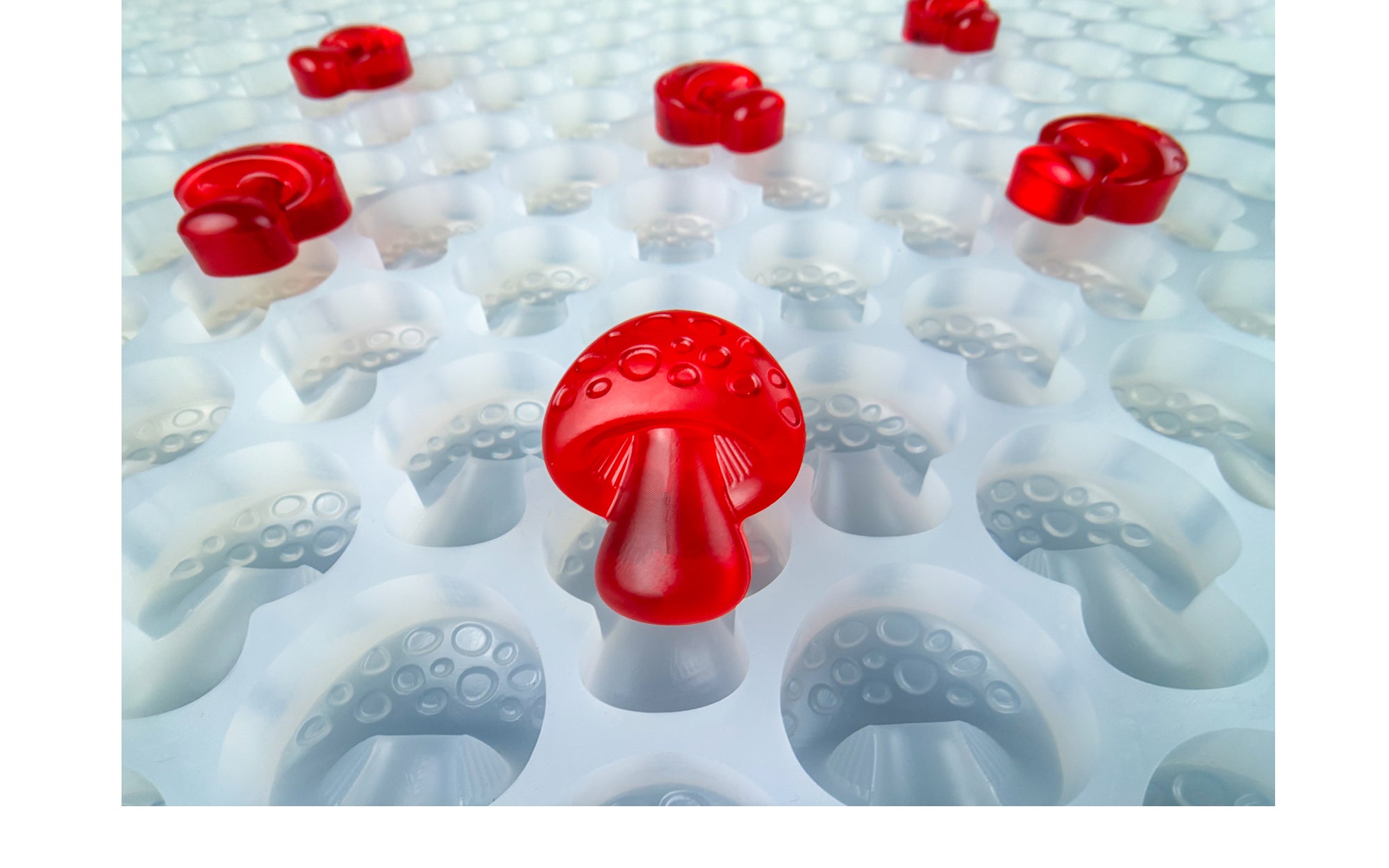 Three red gummy candies shaped like mushrooms rest on a white textured surface with indented circular patterns.