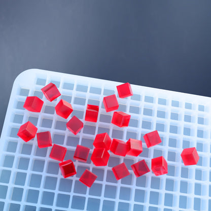 Red gelatin cubes, made with the 1 mL Square & Cube Gummy Mold - Full Sheet (1781 Cavities) by Vector Molds, are scattered on a white plastic grid tray against a blue background.